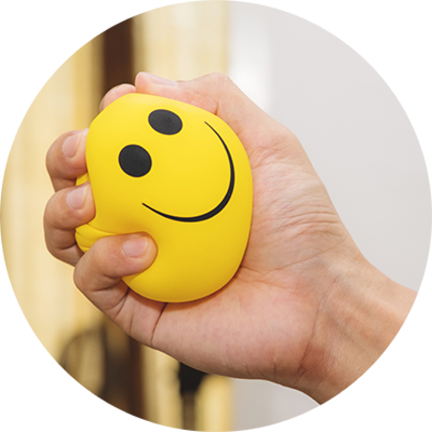 Hand squeezing yellow stress bal with happy smiley face